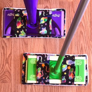 May include: Two Swiffer Sweeper mop heads with a black background and colorful cat print. The top mop head is purple and the bottom mop head is green.
