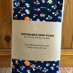 May include: Two reusable wet/dry mop pads with a mushroom print on a dark blue background. The pads are packaged with a brown paper label that reads "Reusable Mop Pads" and "Eco-friendly wet/dry mop pads" and "by PNWbusybobbin.etsy.com *always made with love*"