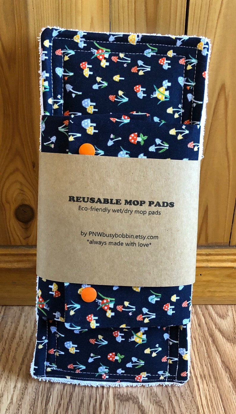 May include: Two reusable wet/dry mop pads with a mushroom print on a dark blue background. The pads are packaged with a brown paper label that reads "Reusable Mop Pads" and "Eco-friendly wet/dry mop pads" and "by PNWbusybobbin.etsy.com *always made with love*"