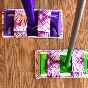 May include: Two Swiffer mop heads with purple and white tie-dye fabric covers. The mop heads are attached to the Swiffer mop handles.