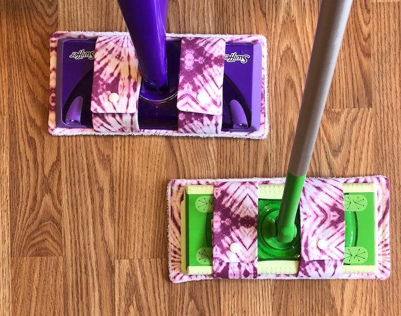 May include: Two Swiffer mop heads with purple and white tie-dye fabric covers. The mop heads are attached to the Swiffer mop handles.