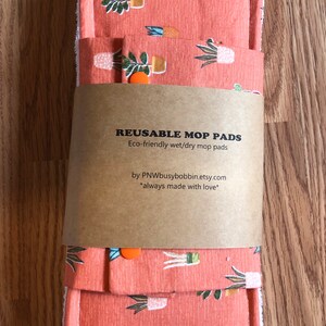 May include: Two reusable mop pads with a terracotta colored fabric featuring a white and green potted plant pattern. The pads are packaged with a brown paper label that reads "REUSABLE MOP PADS Eco-friendly wet/dry mop pads by PNWbusybobbin.etsy.com *always made with love*"