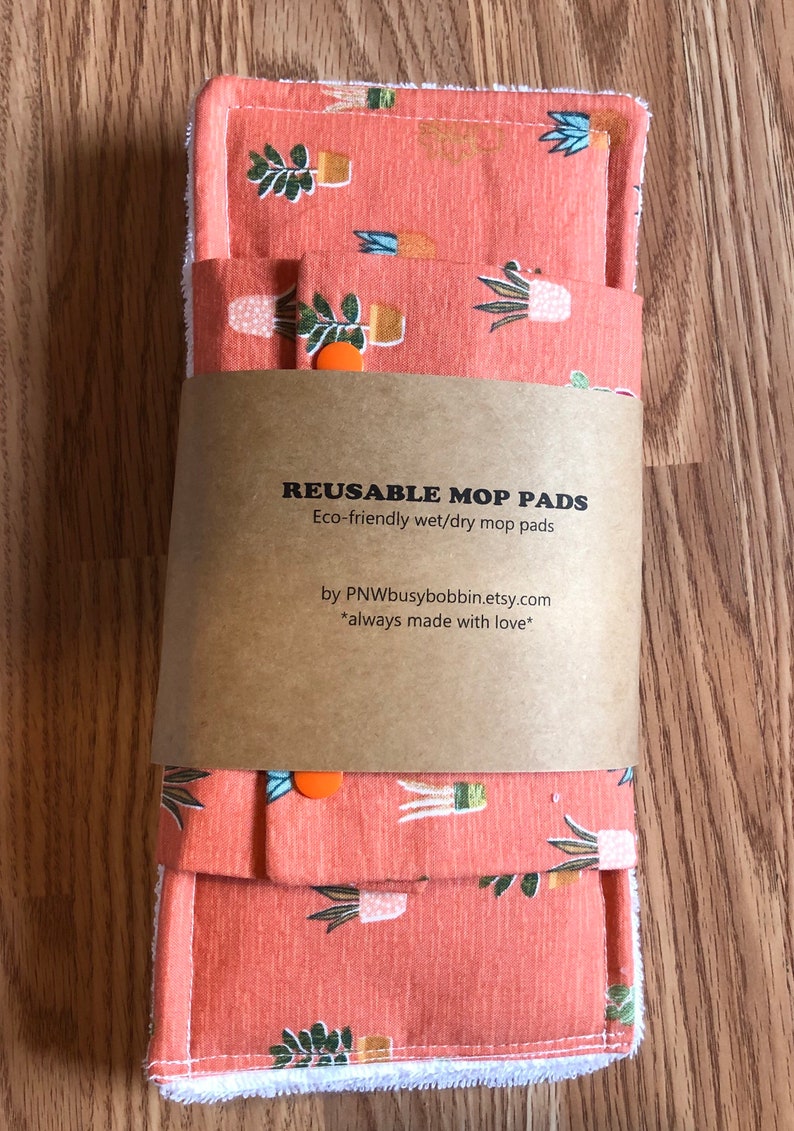 May include: Two reusable mop pads with a terracotta colored fabric featuring a white and green potted plant pattern. The pads are packaged with a brown paper label that reads "REUSABLE MOP PADS Eco-friendly wet/dry mop pads by PNWbusybobbin.etsy.com *always made with love*"
