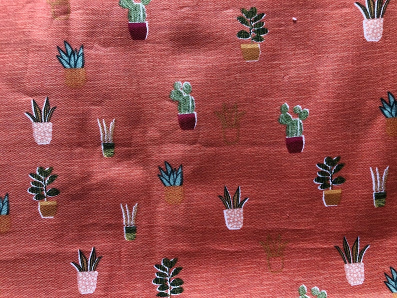 May include: A red fabric with a repeating pattern of potted plants. The plants are green and brown and are in various shapes and sizes. The fabric has a subtle texture.