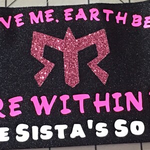 K&ouml;nnte beinhalten: Schwarzes Stoffarmband mit pinkfarbenem Glitzer-Schriftzug "SKY ABOVE ME, EARTH BELOW ME. FIRE WITHIN ME SOLE SISTA'S SO CAL". Das Armband hat ein pinkfarbenes Glitzer-Logo in der Mitte.