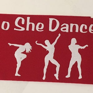 K&ouml;nnte beinhalten: Roter Stoffbanner mit wei&szlig;em Text "So She Dances" und drei wei&szlig;en Silhouetten von T&auml;nzern.