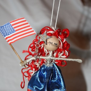 May include: A handmade doll with red and white yarn hair, a blue and silver dress, and a red, white, and blue plaid skirt. The doll is holding a small American flag.