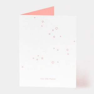 May include: A white card with a pink envelope. The card has a scattering of small pink stars and the text "YOU ARE MAGIC" in pink.