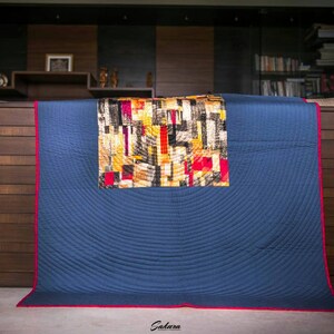 May include: A blue quilted throw blanket with a red border. The blanket has a geometric pattern in shades of yellow, red, and black in the center.