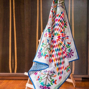 May include: A quilt featuring a central star pattern composed of multicolored diamond shapes in shades of red, orange, yellow, green, blue, and purple. The quilt has a light gray background with floral vine motifs and a solid blue border trim.