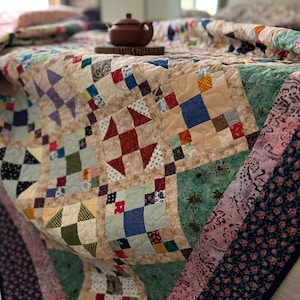May include: A handmade quilt with a patchwork design in various colors, including beige, red, blue, and green. The quilt features the text "GATEWAY scrappy quilt pattern" and "NEW PATTERN IN SHOP". A brown teapot sits on top of the quilt.