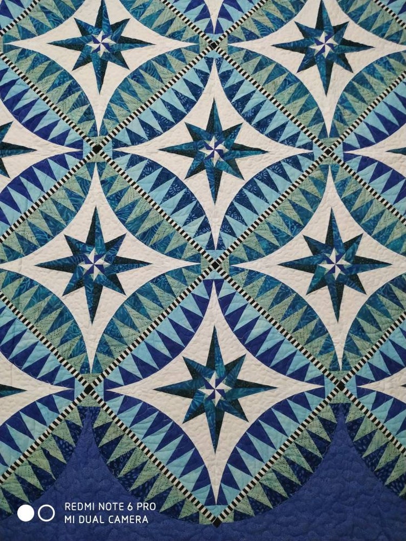 May include: A quilt with a repeating pattern of blue and white stars. The stars are surrounded by a geometric pattern of blue and white triangles.