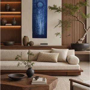 May include: A rectangular indigo blue wall hanging featuring a circular pattern and vertical textured lines created with a tie-dye technique. The fabric is displayed vertically against a neutral wall, showcasing deep blue tones and white resist-dyed details.