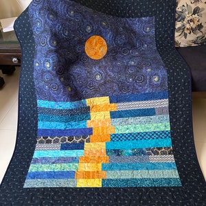 Pode incluir: Uma colcha azul e amarela com um desenho de noite estrelada e um grande círculo laranja no centro. A colcha é feita de vários tecidos e tem uma borda preta.