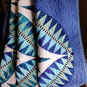 May include: A blue and white quilt with a geometric pattern. The quilt is folded in half and the fabric is textured.