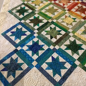 Puede incluir: Una colcha colorida con un diseño de patchwork que presenta una variedad de formas de estrellas en diferentes colores. La colcha está hecha con un fondo blanco y tiene un patrón acolchado.
