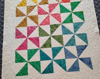 May include: A white quilt with a pattern of colorful pinwheels. The pinwheels are made of fabric in shades of yellow, orange, red, pink, green, blue, and purple. The quilt is quilted with a simple stitch pattern.