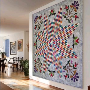 May include: A large wall quilt featuring a central multi-colored star pattern composed of small diamond-shaped fabric pieces. The star is set against a light gray background with floral motifs in the corners, including purple and red flowers.