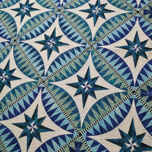 May include: A quilt with a repeating pattern of blue and white stars. The stars are surrounded by a blue and white geometric pattern.