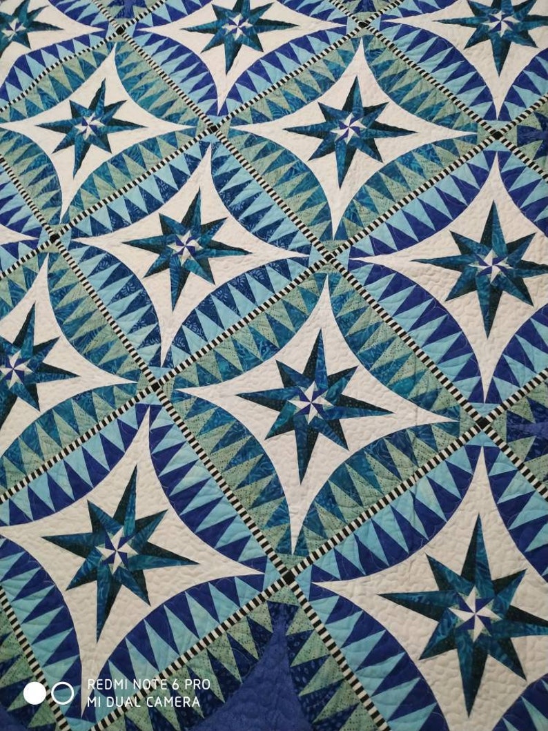 May include: A quilt with a repeating pattern of blue and white stars. The stars are surrounded by a blue and white geometric pattern.