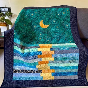 Könnte beinhalten: Eine blaugrüne und marineblaue Steppdecke mit einem Halbmond- und Sternenmuster. Die Steppdecke ist aus Patchwork-Stoff gefertigt und hat eine gesteppte Textur.