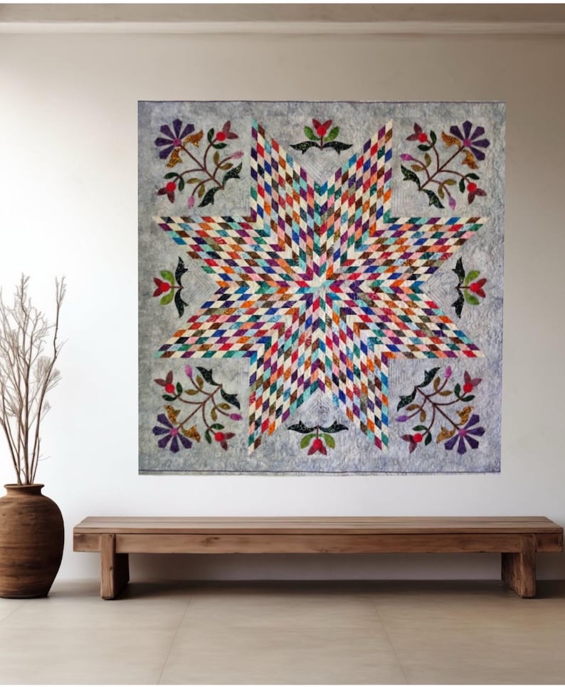May include: A square wall quilt featuring a large central eight-pointed star composed of small, multi-colored diamond-shaped fabric pieces. The background is a light gray fabric, accented with floral motifs in the corners and along the edges.