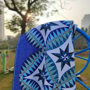May include: A blue and white quilt with a star pattern. The quilt is folded and draped over a blue metal chair.