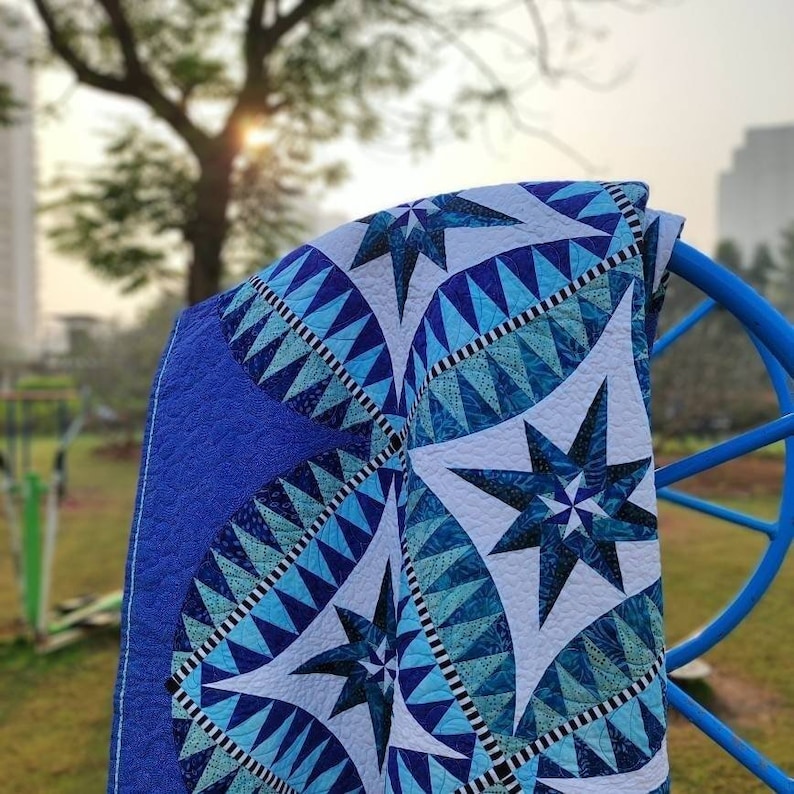 May include: A blue and white quilt with a star pattern. The quilt is folded and draped over a blue metal chair.