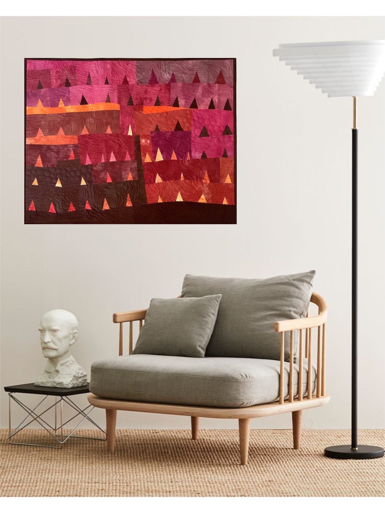 Op de afbeelding: Een grijze fauteuil met een houten frame en een lichtgrijs kussen. De fauteuil staat voor een witte muur met een kleurrijk abstract kunstwerk dat eraan hangt. Een wit buste van een man staat op een kleine tafel links van de fauteuil. Een hoge staande lamp met een witte kap staat rechts van de fauteuil.