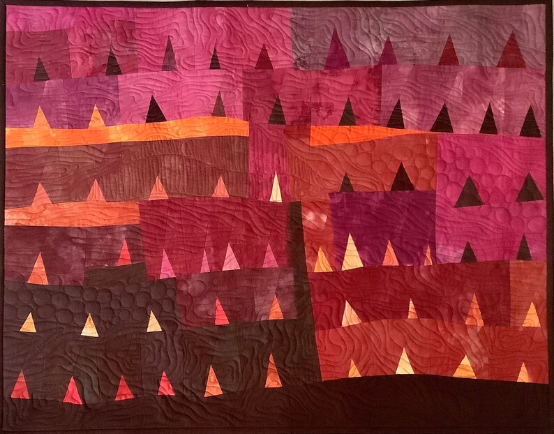 Op de afbeelding: Een quilt met een geometrisch patroon van driehoeken in tinten bruin, rood en oranje. De driehoeken zijn gerangschikt in rijen en kolommen, waardoor een gevoel van diepte en beweging ontstaat.