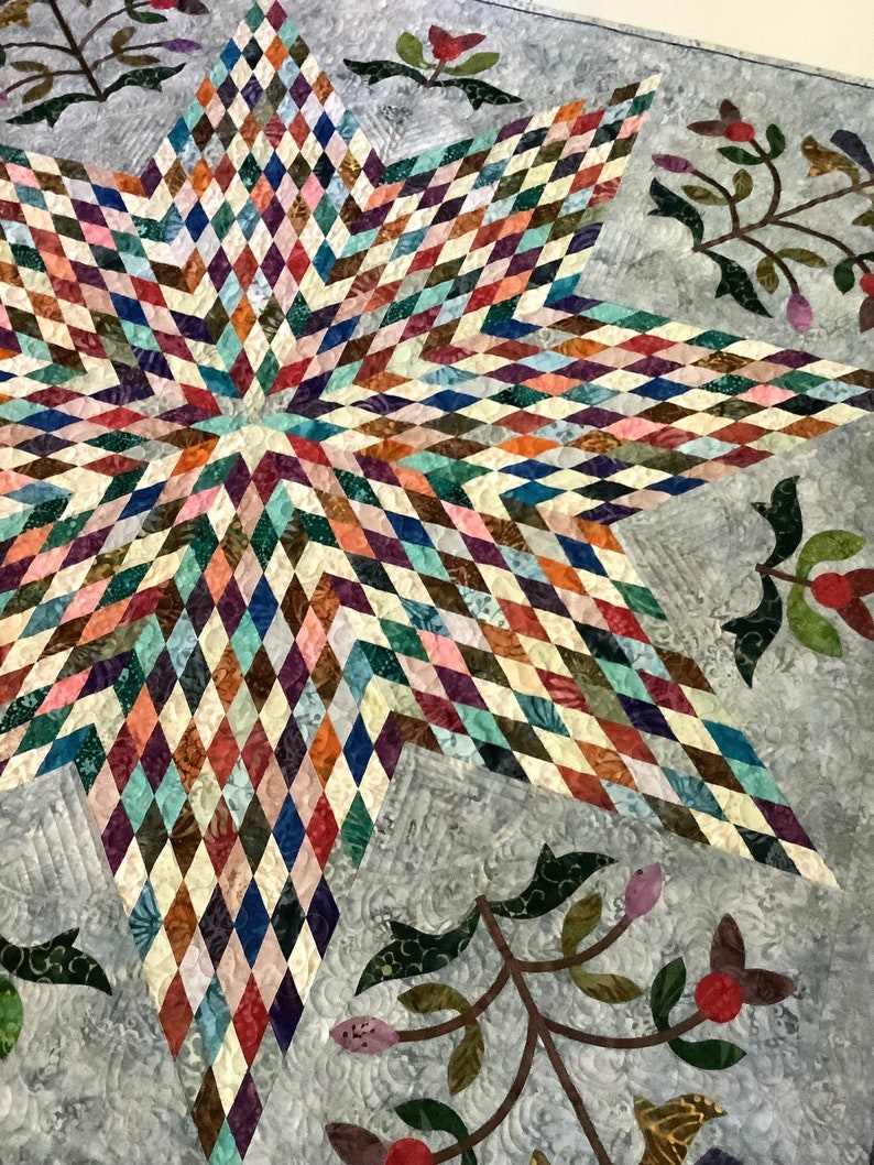 May include: A quilt featuring a large central star composed of numerous small, multicolored diamond-shaped fabric pieces in shades of red, blue, green, and brown, set against a light gray background with floral vine appliques.