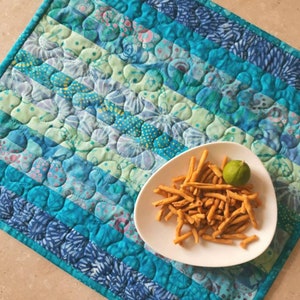 May include: A blue and green quilted table runner with a white plate of fried snacks and a lime wedge on top.