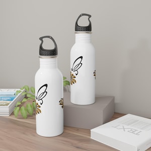 Puede incluir: Dos botellas de agua de acero inoxidable con tapas negras y asas de transporte. Ambas botellas presentan un diseño de mariposa negro y dorado.
