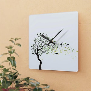 Puede incluir: Un reloj cuadrado blanco con agujas negras y una silueta negra de un árbol con hojas verdes que se mecen con el viento. El reloj tiene un fondo blanco y el árbol está en el centro de la esfera del reloj.