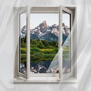 Op de afbeelding: Een open wit raam toont een berglandschap met besneeuwde toppen. Groene bomen en een meer weerspiegelen de bergen. Het raam staat tegen een getextureerde, lichtgrijze muur.
