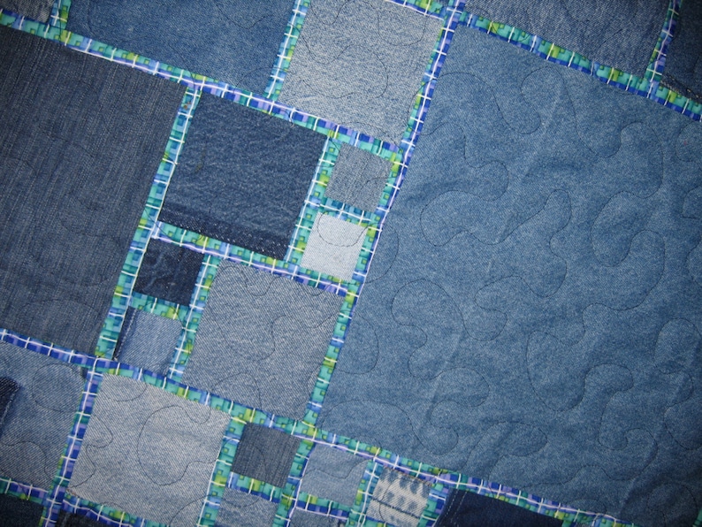 May include: A blue denim quilt with a patchwork design. The quilt is made of different shades of blue denim and is quilted with a wavy pattern.