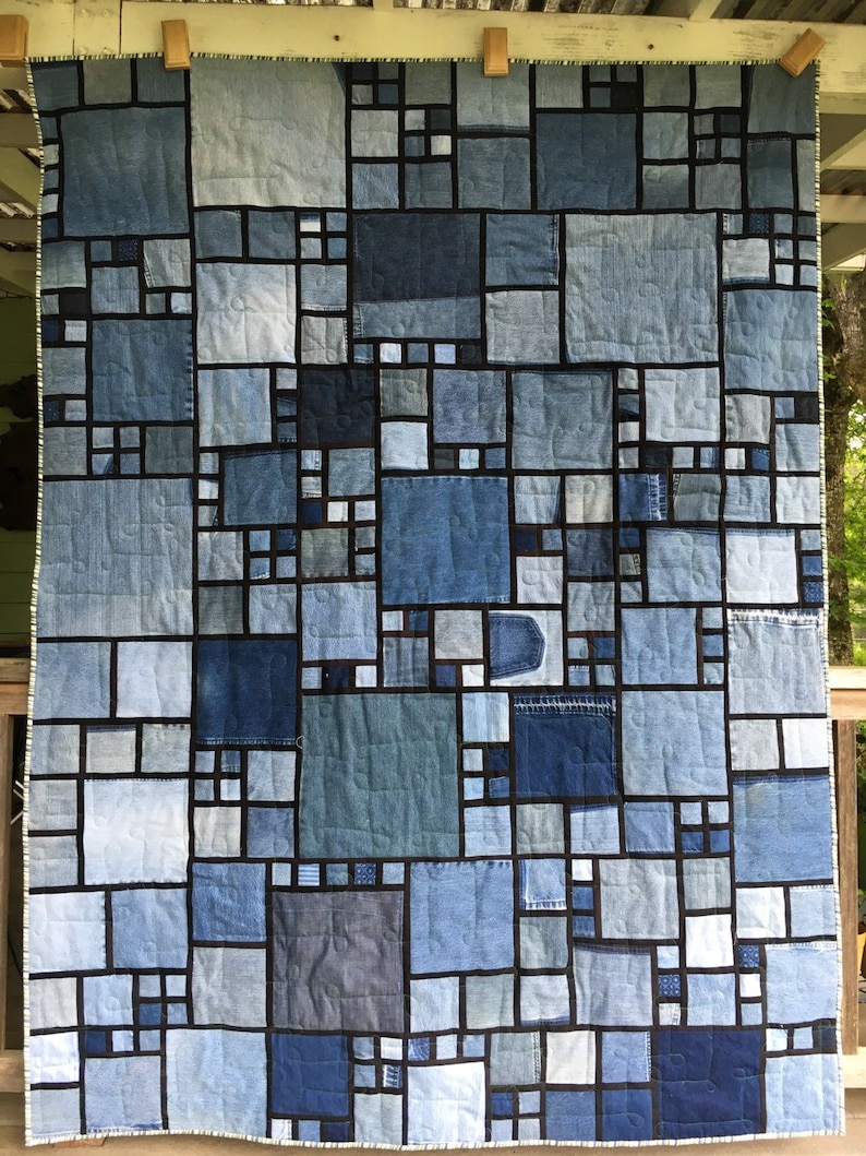 May include: A quilt made from denim fabric in various shades of blue. The quilt is made up of squares of different sizes, each with a black border. The quilt is hanging on a wooden wall.