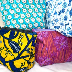 May include: Four quilted fabric pouches with zippered closures. One is bright turquoise with a spool pattern, one is white with blue mystical icons, one is yellow with a dark blue leaf print, and one is magenta with a purple floral pattern.