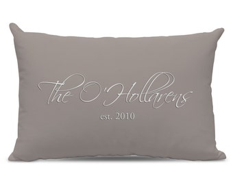 May include: A rectangular, grey-brown cushion featuring the white script text "The O'Hollarens" and the date "est. 2010". The cushion has a plain, solid colour and a soft, inviting appearance.