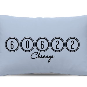 Könnte beinhalten: Ein hellblaues Kissen mit schwarzem Text, der "60622 Chicago" lautet. Die Zahlen sind in Kreisen mit einem abgenutzten Look.