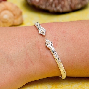 May include: A silver bracelet with a floral design. The bracelet is open and has a delicate, intricate pattern.