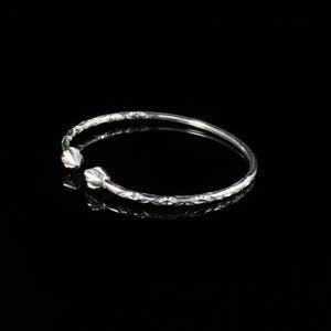 May include: A silver bangle bracelet with a diamond pattern and a rounded end. The bracelet is on a black background.