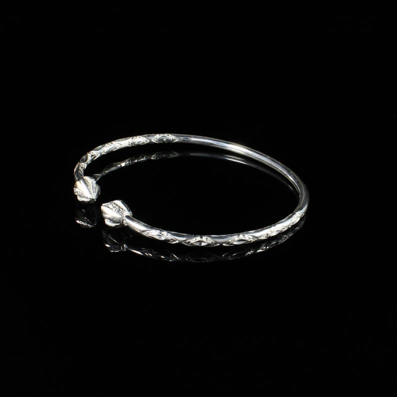 May include: A silver bangle bracelet with a diamond pattern and a rounded end. The bracelet is on a black background.