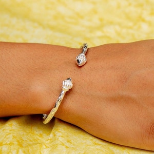 May include: A silver bangle bracelet with a decorative design and a pointed end. The bracelet is open and has a simple, elegant design.