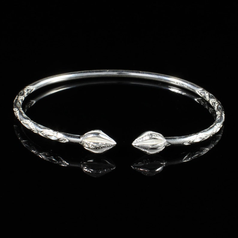 May include: A silver bangle bracelet with a delicate, etched design and pointed ends. The bracelet is open and has a simple, elegant style.