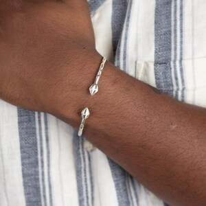 May include: A silver bangle bracelet with a textured design and pointed ends.