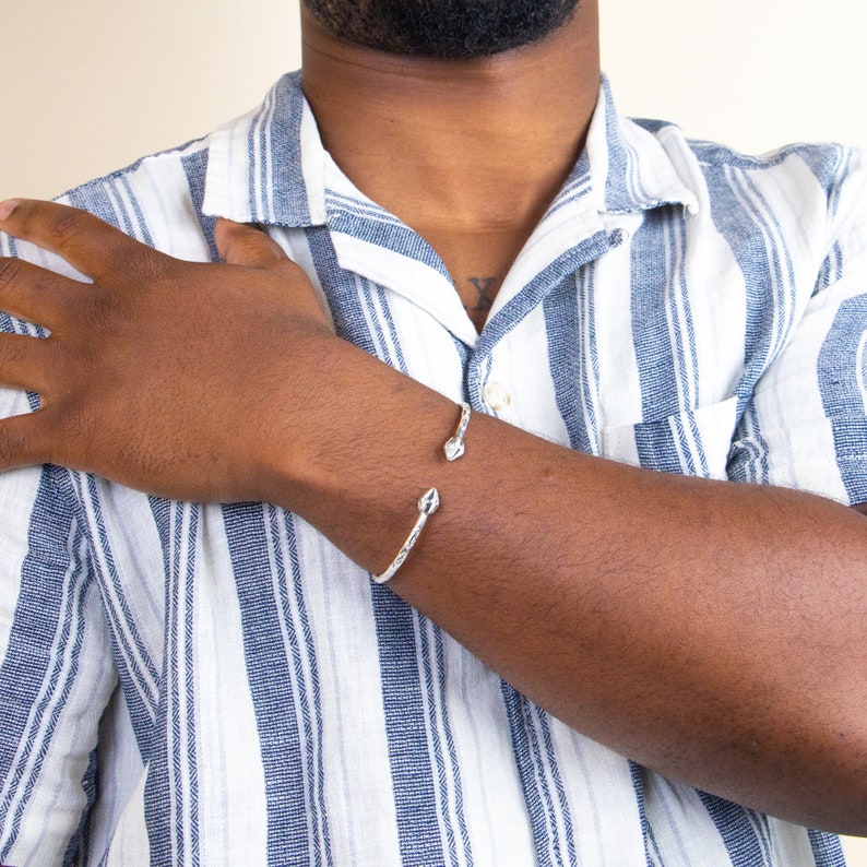 May include: A silver cuff bracelet with a textured design and pointed ends. The bracelet is open and adjustable.