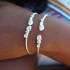 May include: A silver bracelet with three seahorse charms. The bracelet is on a person's wrist.