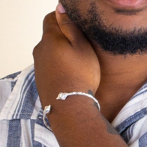 May include: A silver bracelet with a textured design. The bracelet is open and has a curved shape.