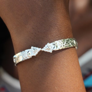 May include: A silver bracelet with a floral design. The bracelet is open and has a delicate, intricate pattern.
